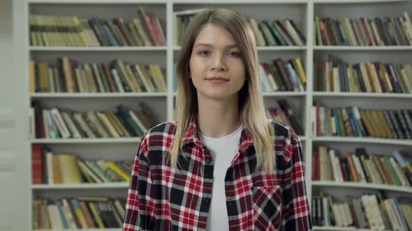 Young Woman in Casual Clothes Standing Near Shelves with Different Books in the Library 