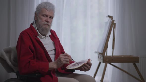 Serious Handicapped Senior Man Looking at Camera Holding Painting Brush and Palette