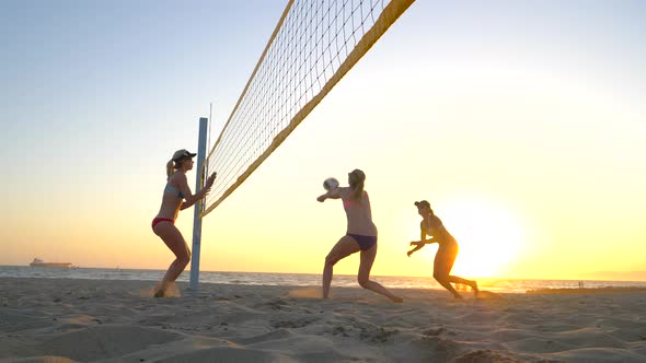 Women players play beach volleyball and a player hitting spiking the ball.