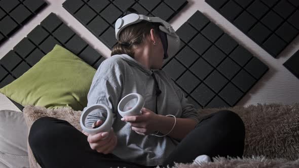 Young Woman Sitting on Sofa Playing Game Using VR Helmet Indoor at Home