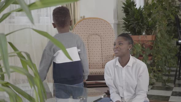 Happy Beautiful African American Woman Playing with Her Little Funny Son on the Cozy Living Room