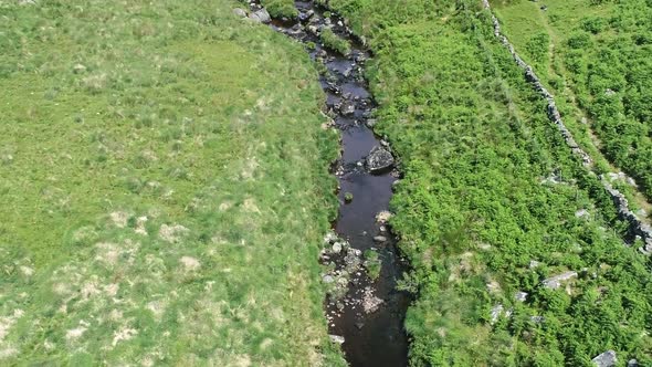 Wide-shot aerial birdseye view tracking forward over a river, with rocks and moorland surround. Dart