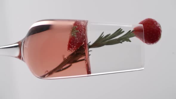 Vertical video: a sprig of rosemary falls in a glass of bubbling champagne with strawberries