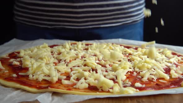 Cooking pizza with tomato sauce and mozzarella cheese. Falling grated cheese. Slow motion.