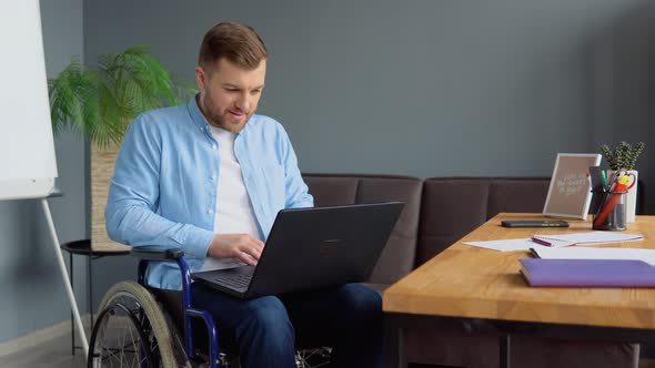 Male Student Learning Online Using Laptop Typing Sitting in Wheelchair in Apartment Busy with