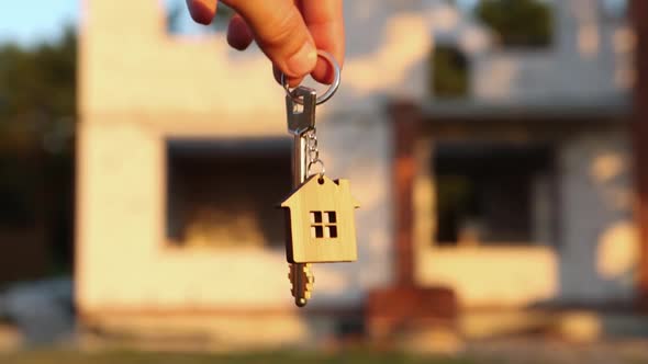 Hand with the key to the future house on the background of a construction site and walls