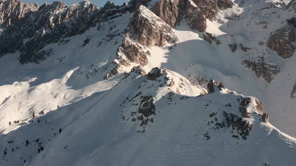 Dolly forward pan up drone shot along snowy mountain ridge towards large rock falls