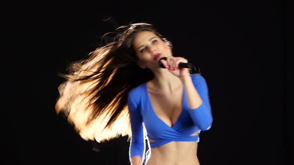 Girl in the Blue Frank Top Sings Into the Microphone. Black Background