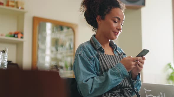 Happy woman barista texting by phone