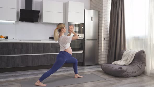 Pregnant Woman in the Halflotus Position Sitting on the Floor on a Fitness Mat is Engaged in