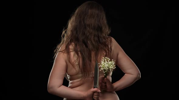 Back View Plus Size Woman in Bra Holding Knife and Bouquet Standing at Black Background