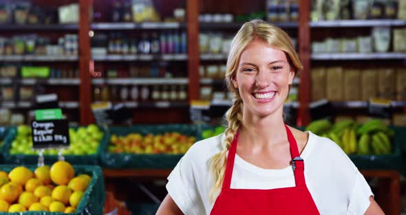  Smiling female staff standing with hands on hip in grocery section