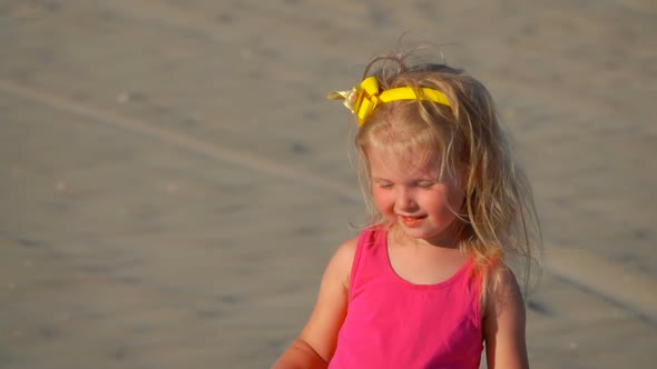 Little Girl in the Pink Skirt is Playing with a Wooden Stick on the Beach