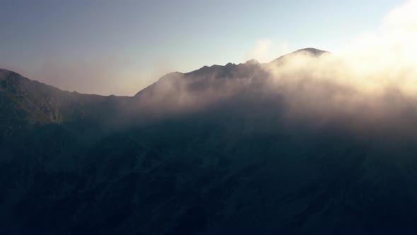 Lifting shot up and over the mountain range flying through the clouds.