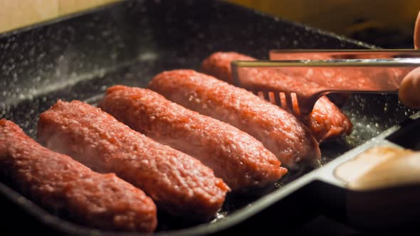 The Cook Returns with Food Tongs the Pink Sausages That are Fried on the Grill Pan