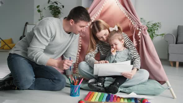 Parenting a Happy Family with a Little Daughter Watching Children's Drawings While Sitting in a