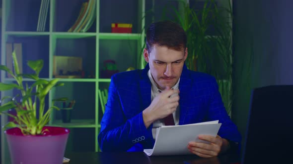 Young Man Examines Documents Sitting in Office