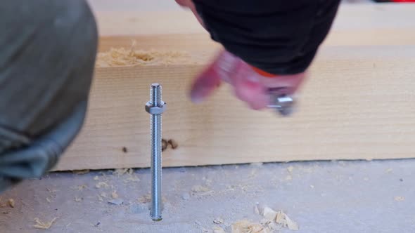 Hands of master twist washer with nut onto a threaded steel stud into concrete floor of rough floor