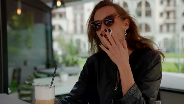 Portrait of a Woman with Bright Lipstick Sunglasses with a Cocktail and a Cigarette in a Street Cafe