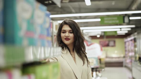 Beautiful Woman Examines the Goods on the Supermarket Shelves and Smiles