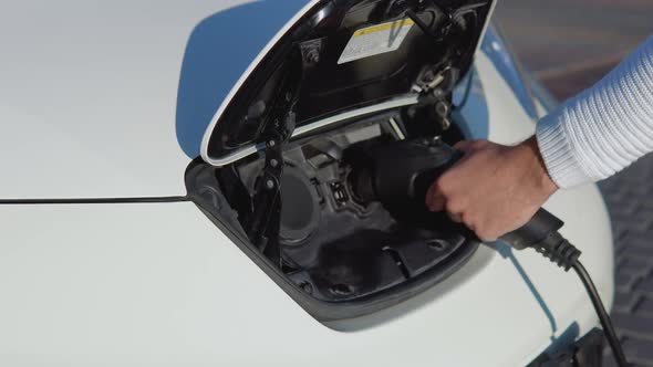A Fairskinned Male Driver Connects Electric Car to Power System to Charge Car Battery