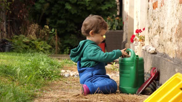 little boy in boots and overalls playing in the garden