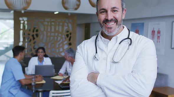 Portrait of caucasian male doctor smiling, with colleagues in discussion in background