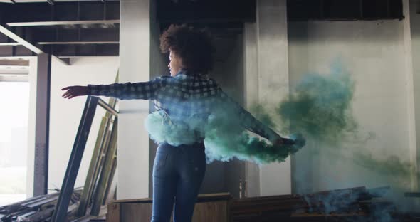 Mixed race woman holding green flare dancing in an empty building