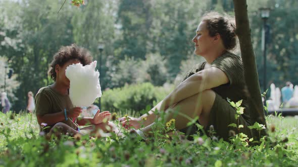 Black Little Girl Eating Cotton Candy in the Park and Her White Mother Sitting in Front of Her