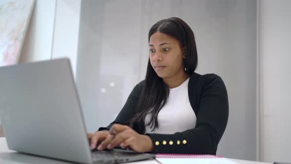 Serious black woman working on laptop in office