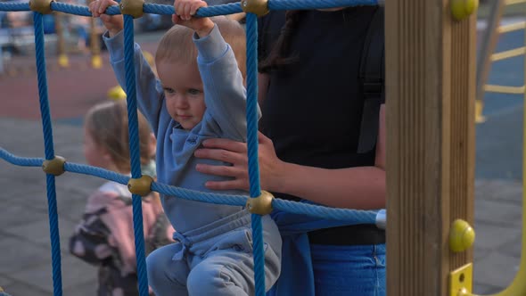 Mother Holds Son Trying to Climb on Metal Construction