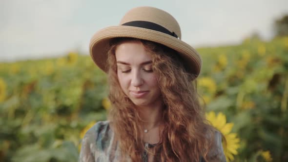 Joyful Girl Undresses Hat and Shakes Her Hair Among Sunflowers Under Bright Sky