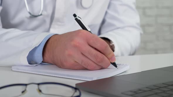 Doctor examines patient online video call laptop writes symptoms in notebook