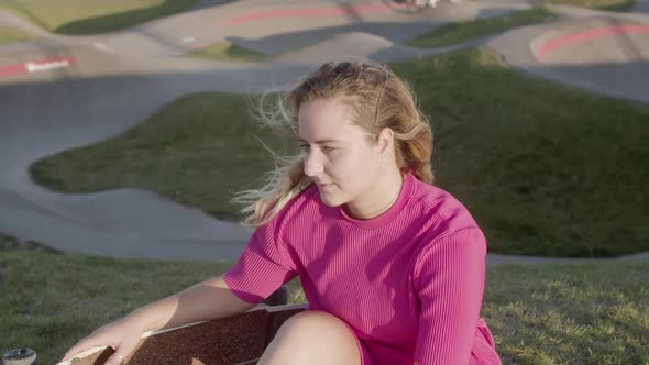 Smiling Girl in Dress Sitting on Lawn in Skate Park