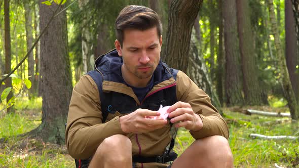 A Young Handsome Hiker Sits on the Ground in a Forest and Blows His Nose with a Handkerchief