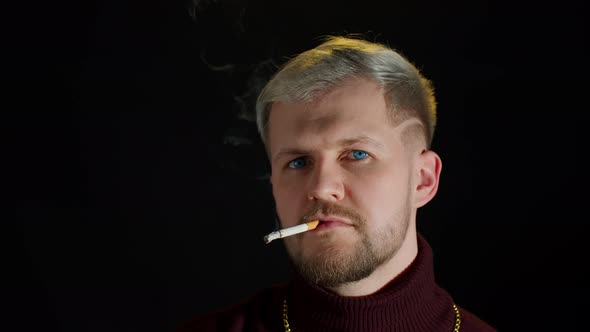 Stylish Addicted Young Man with Blue Eyes in Trendy Clothes Looking at Camera Smoking Cigarette