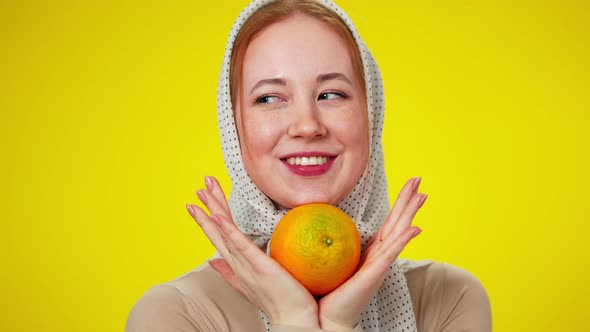 Closeup Portrait of Cheerful Redhead Caucasian Woman in Kerchief Holding Orange Fruit Looking at