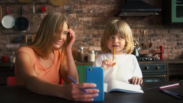 Mother and Son Enjoying Online Video Call on Smartphone While Doing Homework in School Copybook