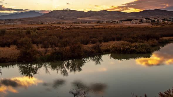 Focusing on the reflective surface of a river then zooming out to reveal a time lapse of a sunset cl