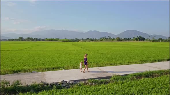 Sise View Drone Flies Along Woman with Girl on Road