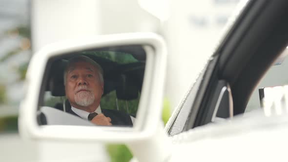 4K Senior businessman sitting in the car straightens his shirt and necktie before driving.