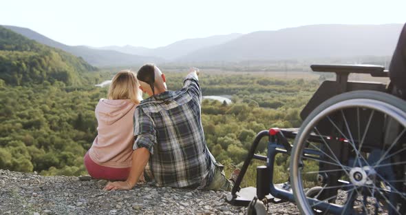 Couple Sitting Near Man's Wheelchair on the Mount on the Wonderful Landscapes Background