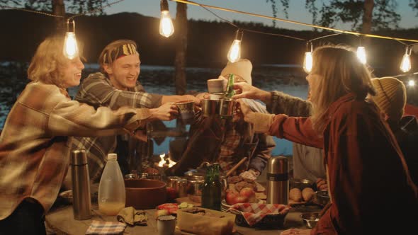 Group of Friends Toasting with Drinks at Camping Dinner