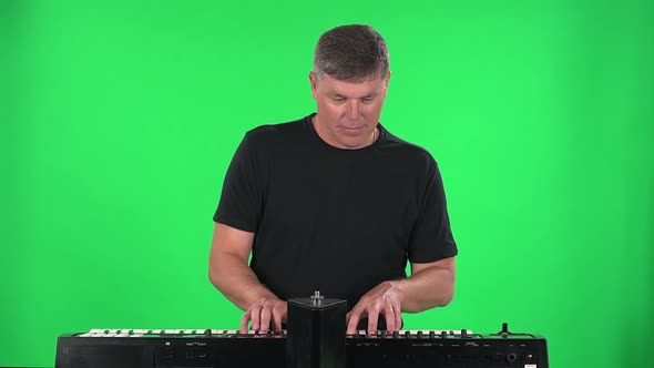 Portrait Musician Is Looking at the Camera and Playing on Synthesizer Piano Keyboard on a Green