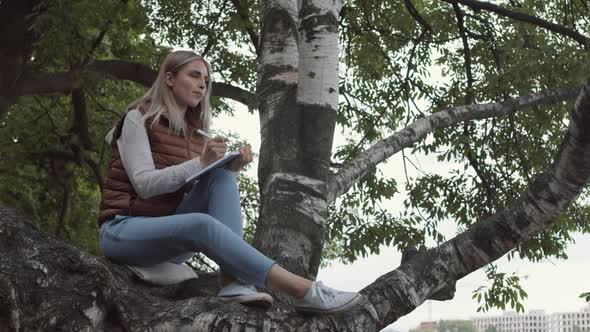 Woman Sitting on Tree and Writing in Notepad
