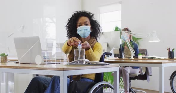 Woman wearing face mask sanitizing her hands at office