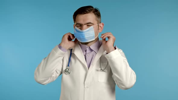Young Doctor Puts on Face Medical Mask During Coronavirus Pandemic. Medical Stuff Portrait on Blue
