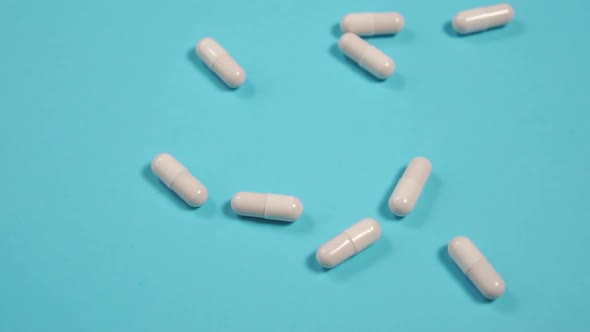 White pills on a blue background. A handful of medical capsules fall on a bright surface