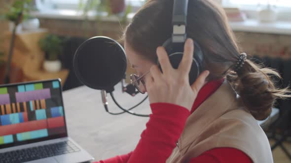 Female Podcaster Putting on Headphones and Taking Notes