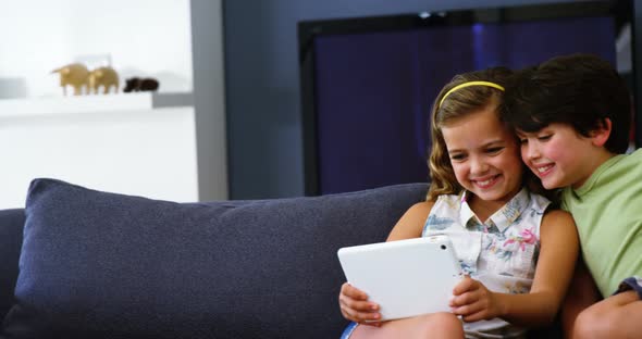 Siblings using digital tablet in living room